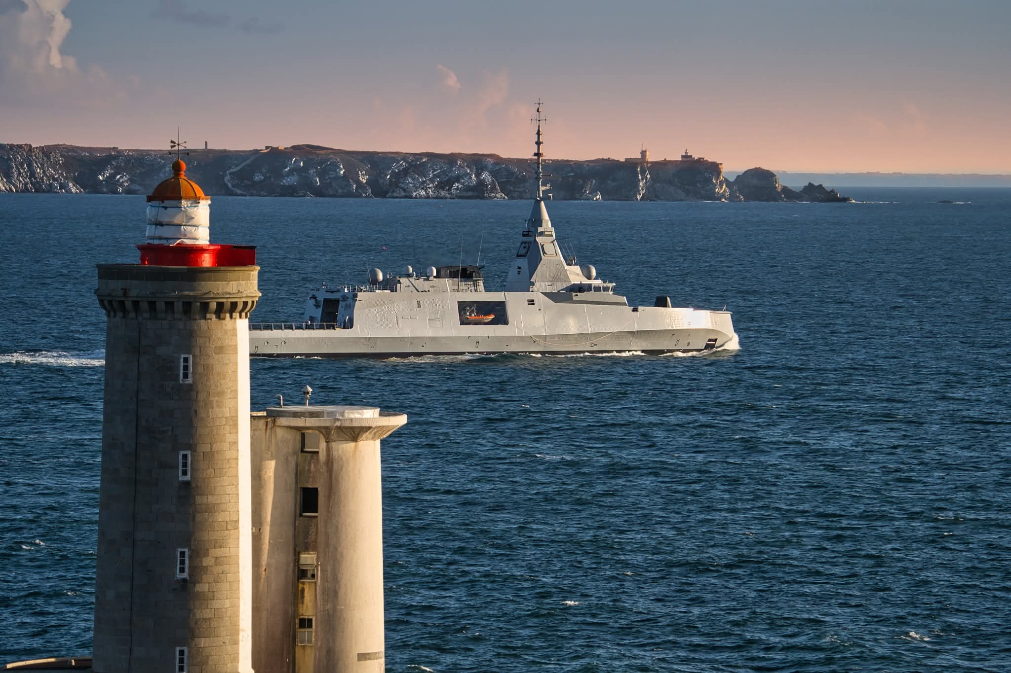 Frégate de Défense et d'Intervention passant devant le phare de Lorient au coucher de soleil